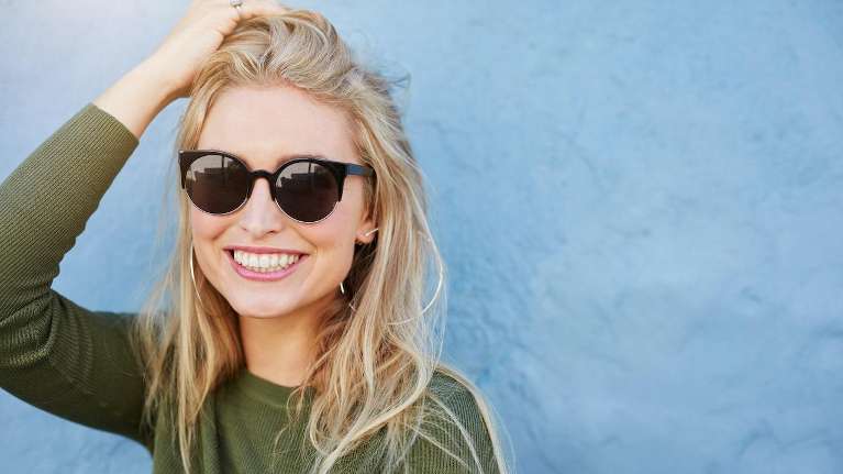 Blonde woman wearing sunglasses smiles with her full set of teeth in Kentucky